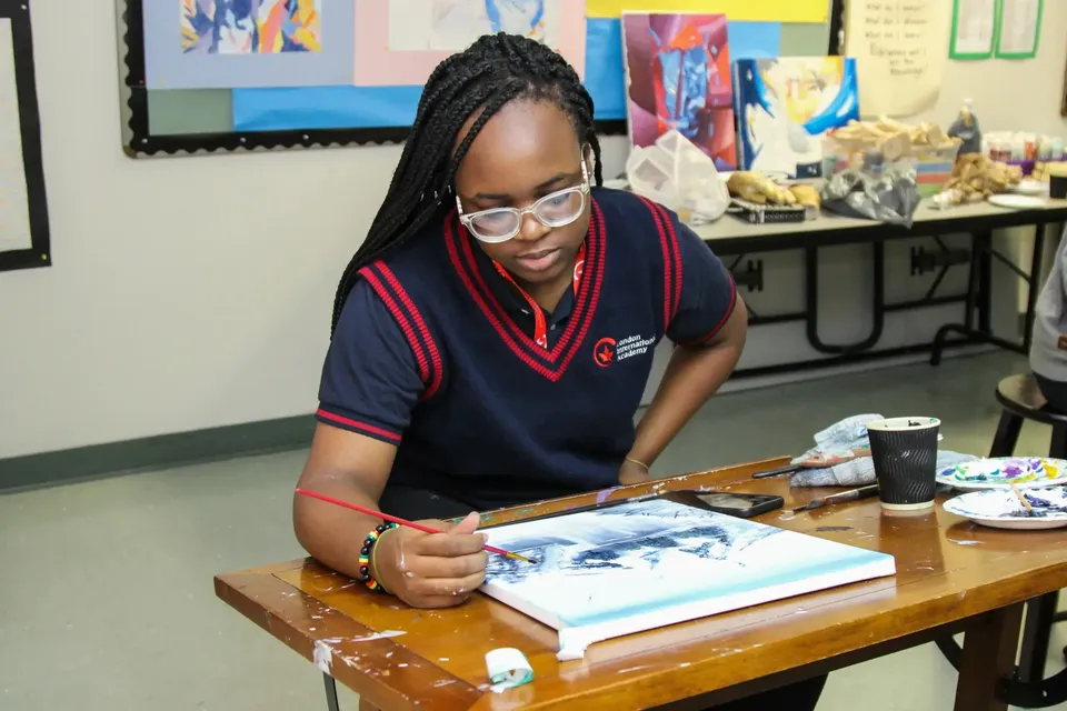 Una studentessa della London International Academy siede concentrata a un tavolo lavorando a un'opera d'arte.