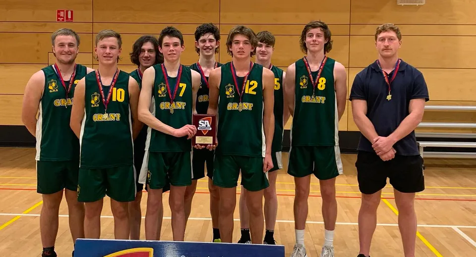 Un gruppo di studenti della Grant High School con canotte da basket verdi posa con una coppa in una palestra.