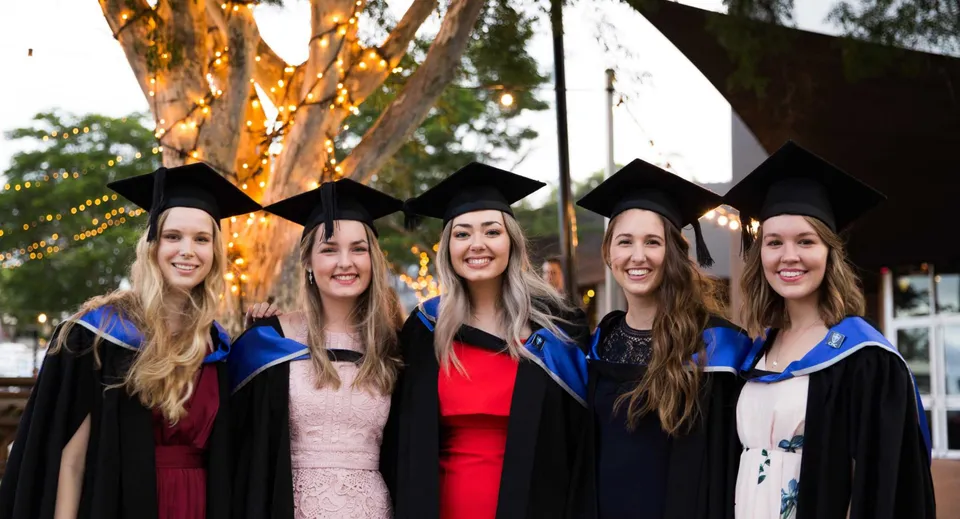 Cinque studentesse in toga da diploma posano insieme davanti a un albero nel campus del Calamvale Community College.