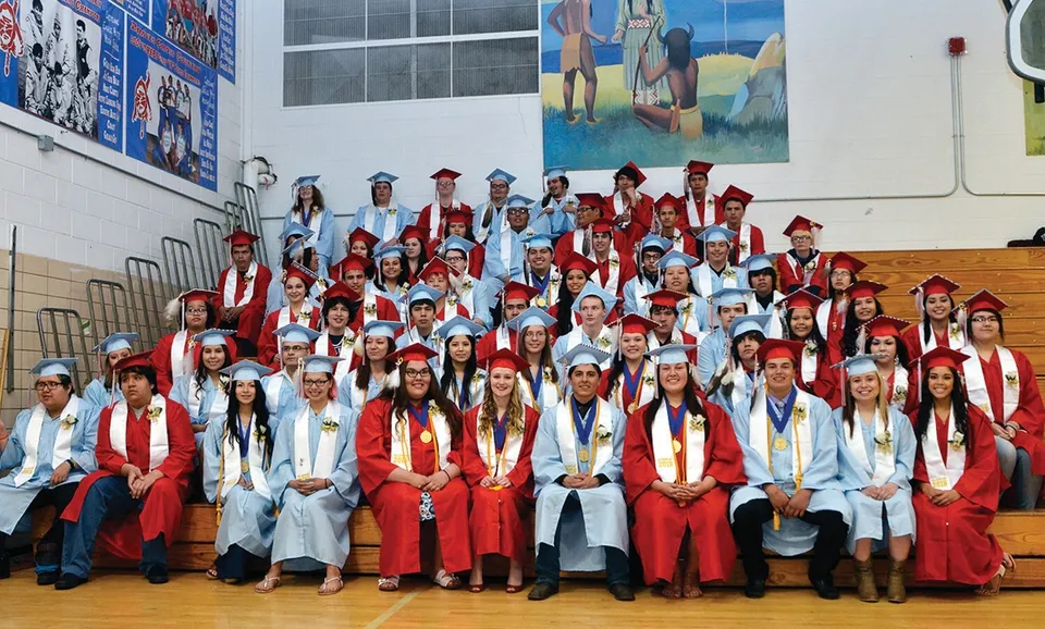 I diplomati della Eagle Butte High School in toga rossa e bianca posano davanti a un murale colorato.