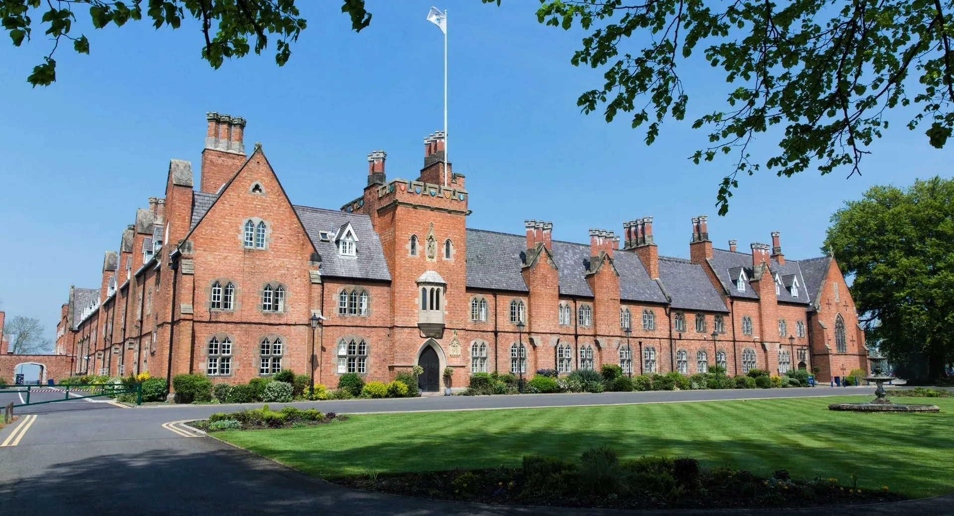 L'imponente edificio in mattoni con torri e camini nel campus del Ratcliffe College è circondato da un prato curato e alberi.
