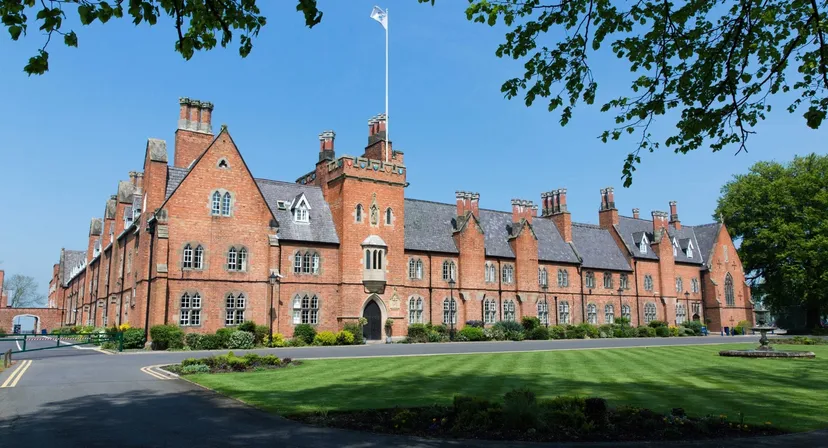 L'imponente edificio in mattoni con torri e camini nel campus del Ratcliffe College è circondato da un prato curato e alberi.