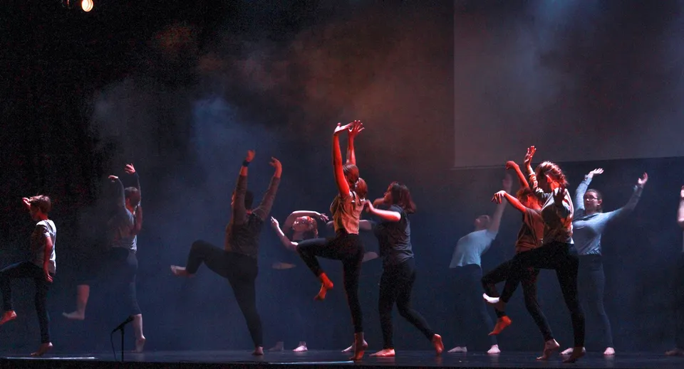 Studenti della Abbotsford School of Integrated Arts durante uno spettacolo di danza su un palco con luci soffuse e nebbia.
