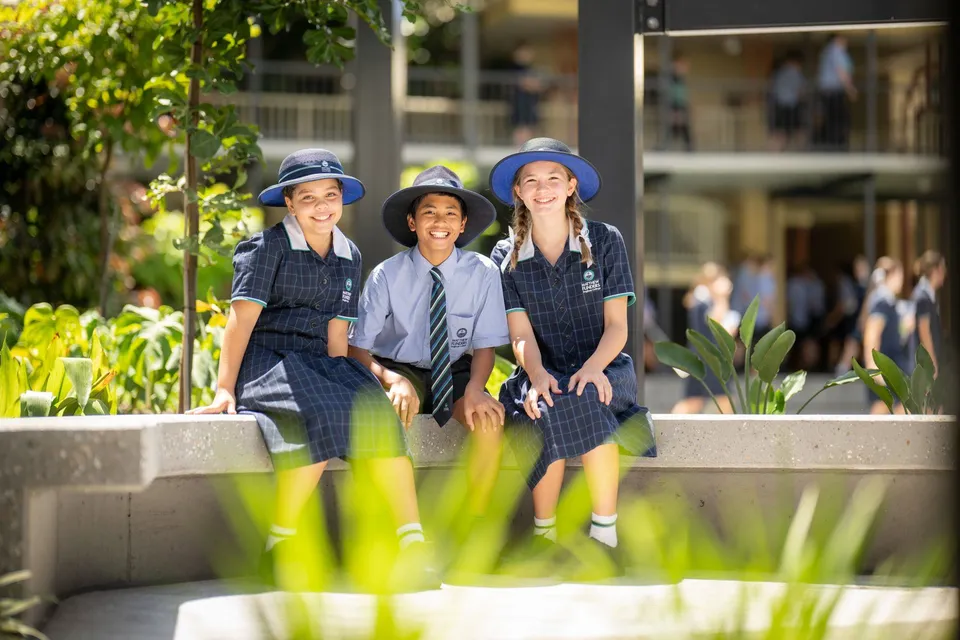 Tre studenti del Matthew Flinders Anglican College posano insieme sorridenti davanti a una cornice vegetale verde.