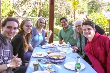 Grupo de personas sonrientes comiendo alrededor de una mesa en un jardín