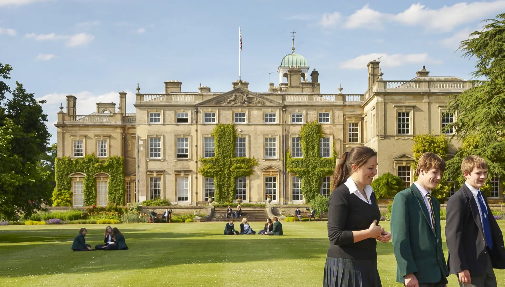 Diverse persone in abiti formali si radunano sul prato davanti all'edificio storico della Culford School.