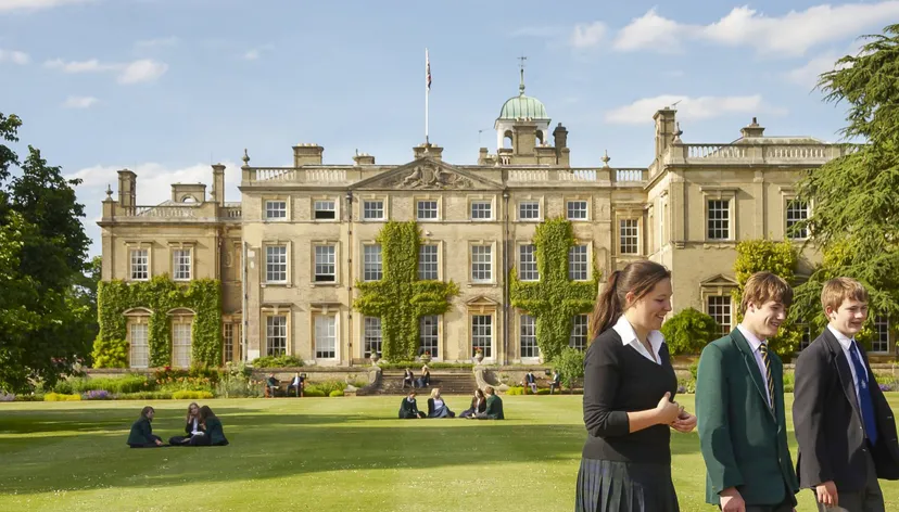 Diverse persone in abiti formali si radunano sul prato davanti all'edificio storico della Culford School.