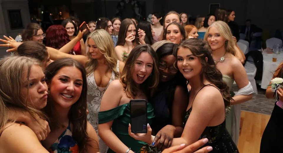 Studentesse della Rockford Manor School in abito da sera festeggiano e scattano una foto con uno smartphone.
