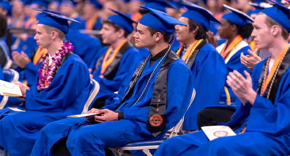 Diplomate e diplomati del Chaffey Joint Union High School District siedono in toga blu durante la cerimonia di diploma nell'auditorium.