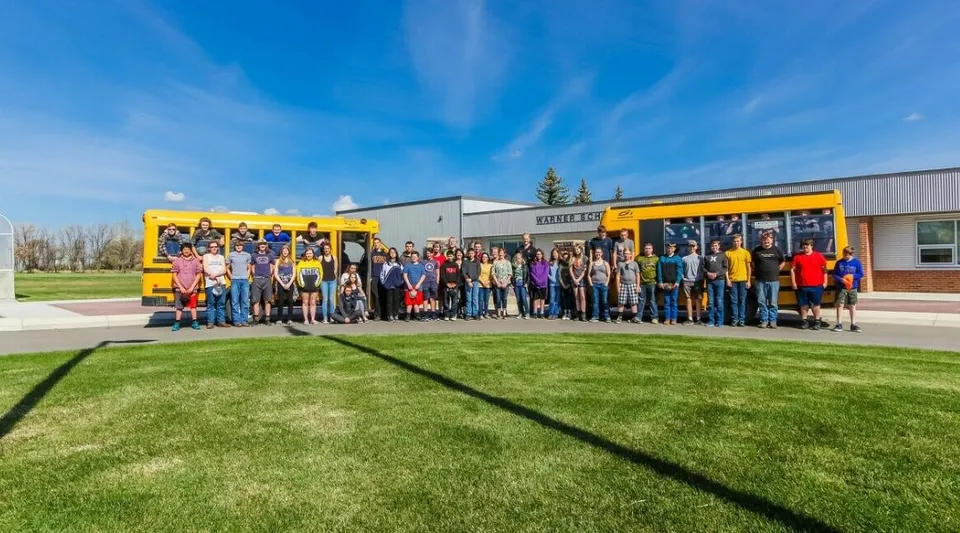 Un gruppo di studenti e adulti è in piedi davanti a uno scuolabus giallo nel campus della Warner School.