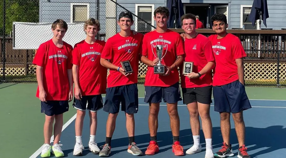 Un gruppo di studenti della Oak Mountain Academy sta sul campo da tennis tenendo dei trofei.