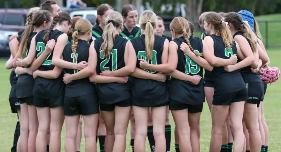 Un gruppo di giovani atlete si trova su un campo sportivo della Ferny Grove State High School davanti ad alberi ed edifici.