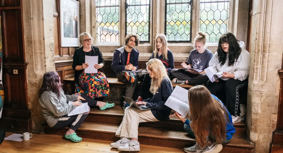 Un gruppo di studenti e studentesse siede sulle scale di un vecchio edificio con vetrate colorate nel campus della Frensham Heights School.