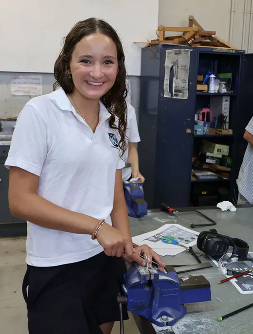 Estudiante con uniforme sonríe durante una clase práctica en el taller del instituto