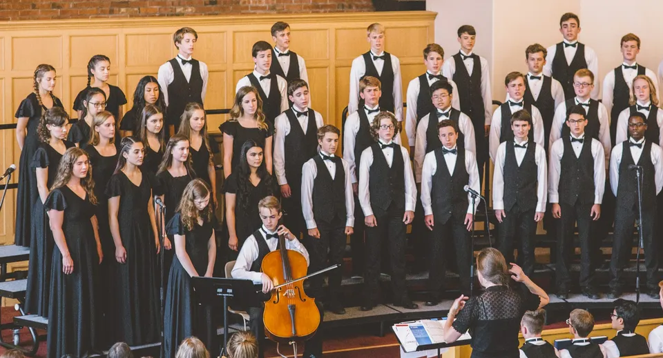Il coro della Covenant High School si esibisce in abito formale, accompagnato da un violoncellista e una direttrice.