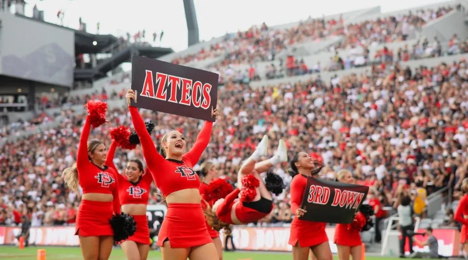 Studenti della San Diego State University fanno il tifo nello stadio con uniformi rosse e abiti da cheerleading.