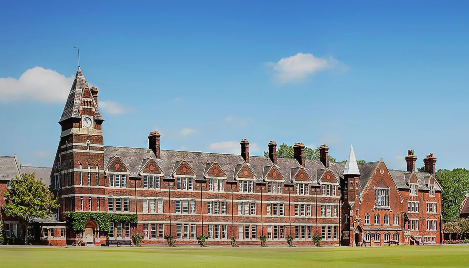 L'edificio storico in mattoni della Felsted School con un'alta torre sorge su un prato sotto un cielo blu.