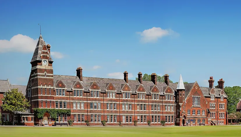 L'edificio storico in mattoni della Felsted School con un'alta torre sorge su un prato sotto un cielo blu.