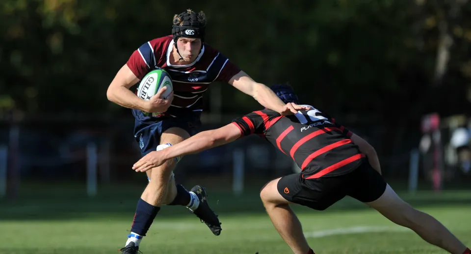 Un giocatore di rugby della Dean Close School corre con la palla su un campo d'erba.