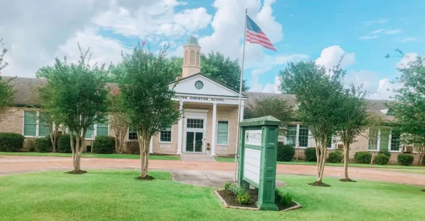 L'edificio della Hamilton Christian Academy con colonne all'ingresso, una bandiera americana e un prato verde.