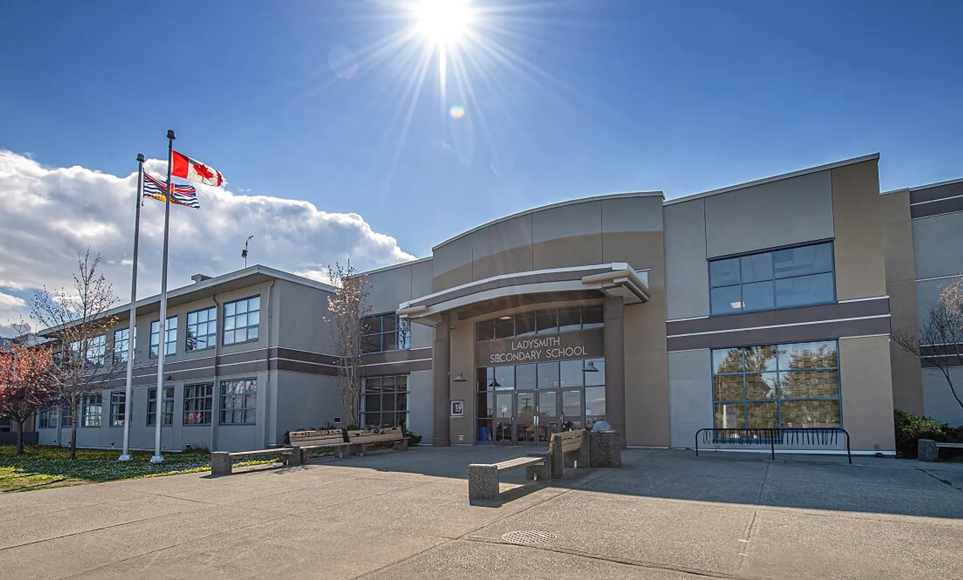 L'edificio moderno a più piani della Ladysmith Secondary School con facciata curvata e bandiere circostanti sotto un sole splendente.