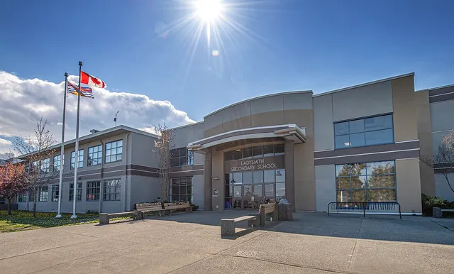 L'edificio moderno a più piani della Ladysmith Secondary School con facciata curvata e bandiere circostanti sotto un sole splendente.