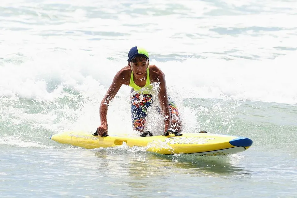 Una persona su una tavola da surf gialla cavalca le onde al largo della costa del Papamoa College.