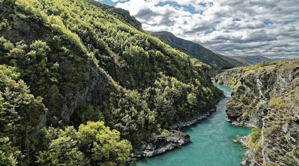 Un paesaggio montano boscoso con un fiume turchese che si snoda tra rocce scoscese.