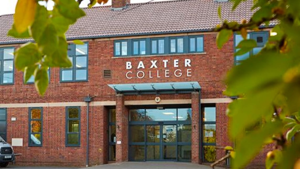 Roter Backsteinbau mit der Aufschrift „Baxter College“ und verglastem Haupteingang, gerahmt von Laub