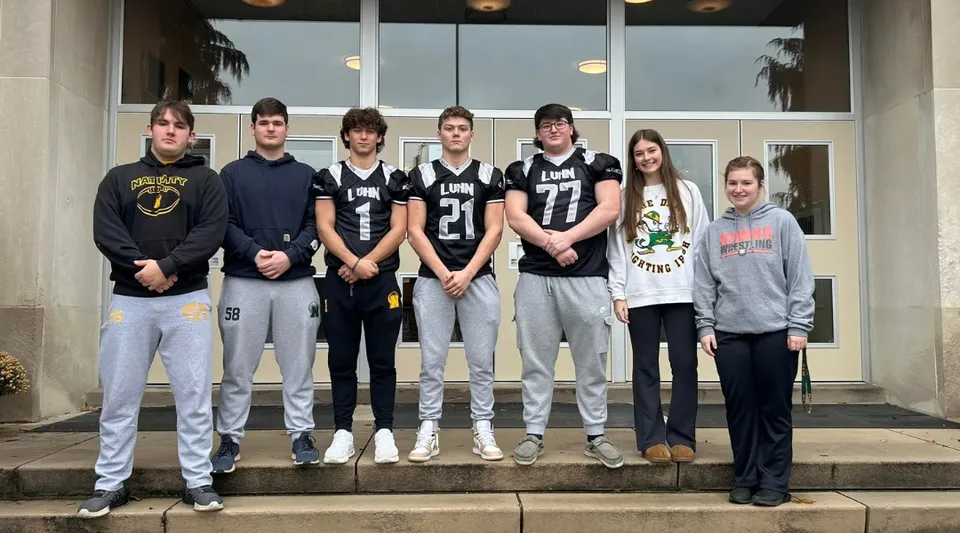 Una squadra sportiva sulle scale davanti all'edificio della Nativity BVM High School con palme sullo sfondo.
