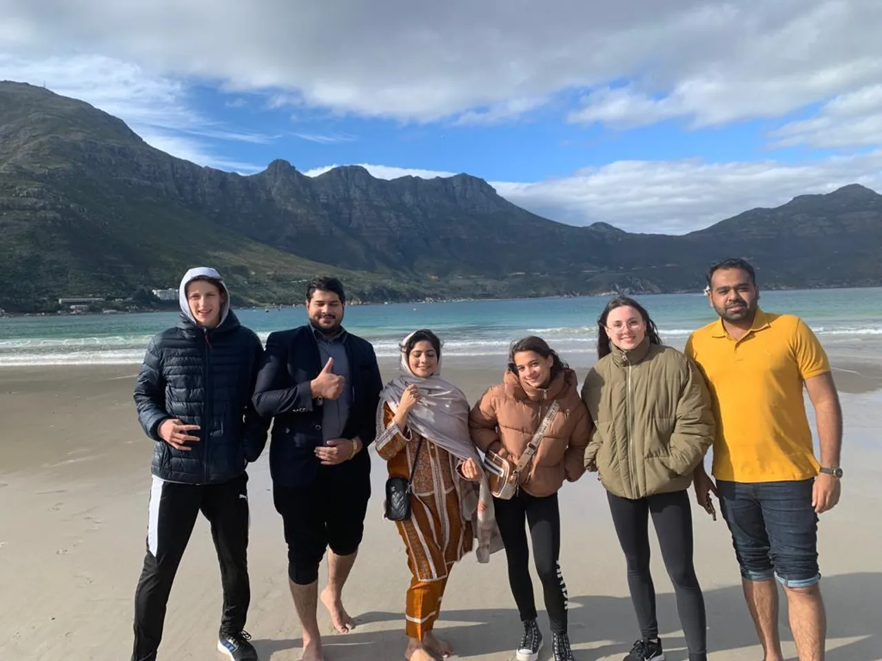 Gruppo di studenti in posa su una spiaggia con le montagne sullo sfondo in Sudafrica