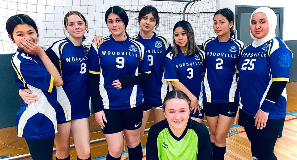 Un gruppo di giovani giocatrici di pallavolo della Woodville High School posa insieme sul campo da pallavolo.