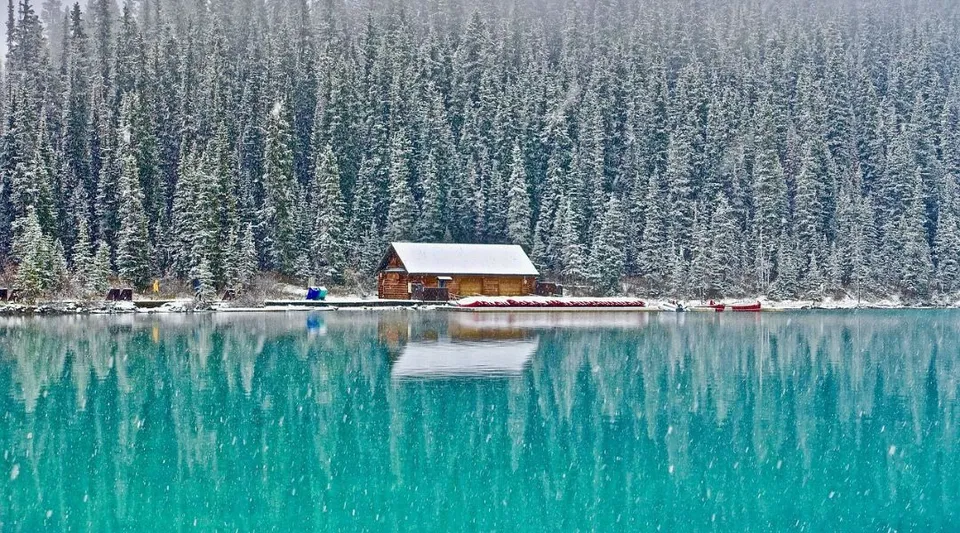 Una piccola capanna di legno si trova sulla riva di un lago turchese davanti a un bosco innevato nella proprietà della Alexander Galt Regional High School.