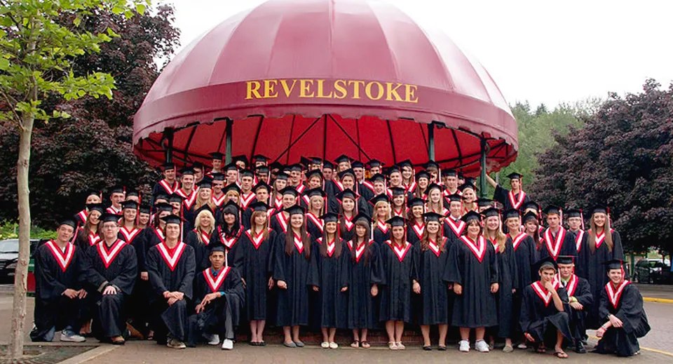 Un gruppo di studenti e studentesse in abito da diploma posa davanti alla grande cupola rossa della Revelstoke Secondary School.