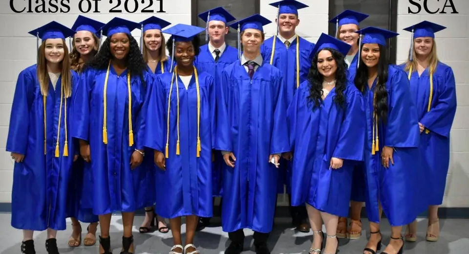 Un gruppo di diplomati della Southwest Christian Academy posa in toga blu davanti a una parete con la scritta Class of 2021.