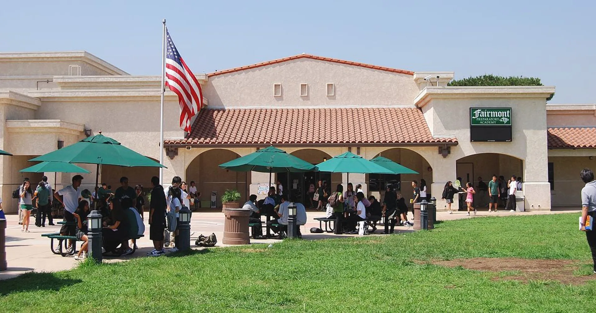 Studenti della Fairmont Prep Academy davanti all'edificio in stile spagnolo con ombrelloni verdi.