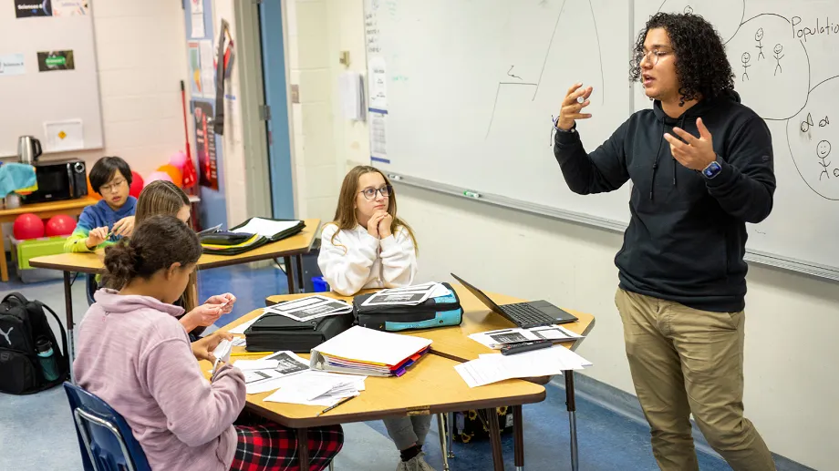 Estudiantes y un docente de las Red Deer Public Schools debaten juntos en el aula con materiales didácticos y tecnología en el fondo.