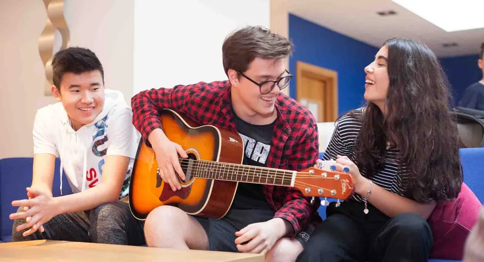 Tre giovani della Westbourne School siedono insieme in una stanza mentre uno di loro suona la chitarra acustica.
