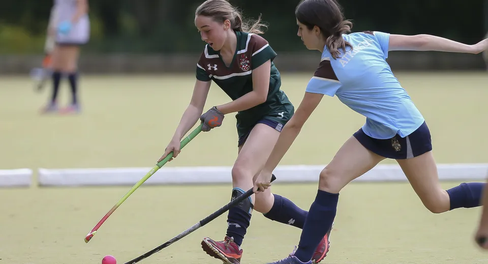 Due atlete della Mill Hill School giocano una partita di hockey su un campo in erba.