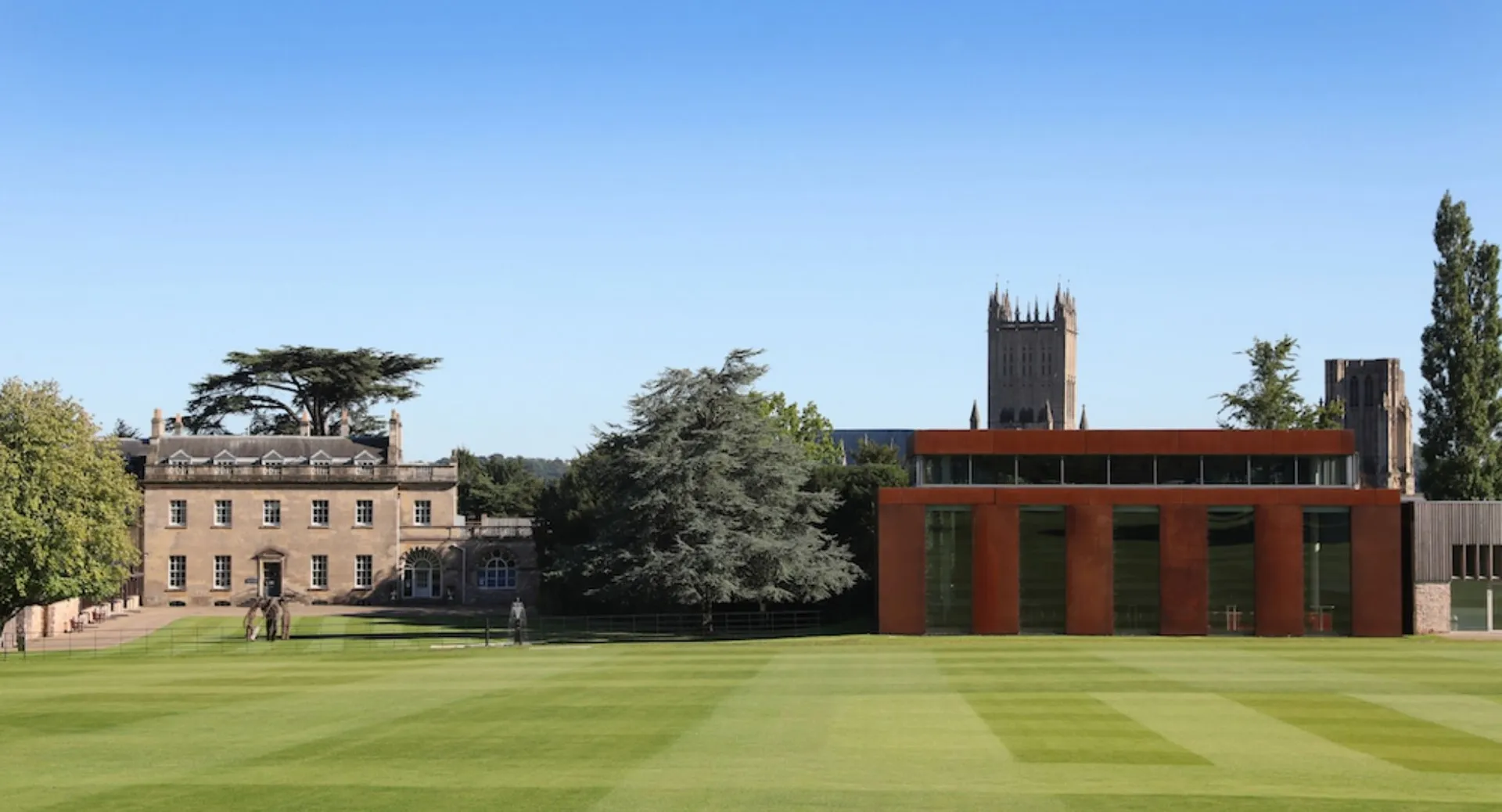 Il verde campus della Wells Cathedral School con edifici storici e una torre moderna sullo sfondo sotto un cielo blu.