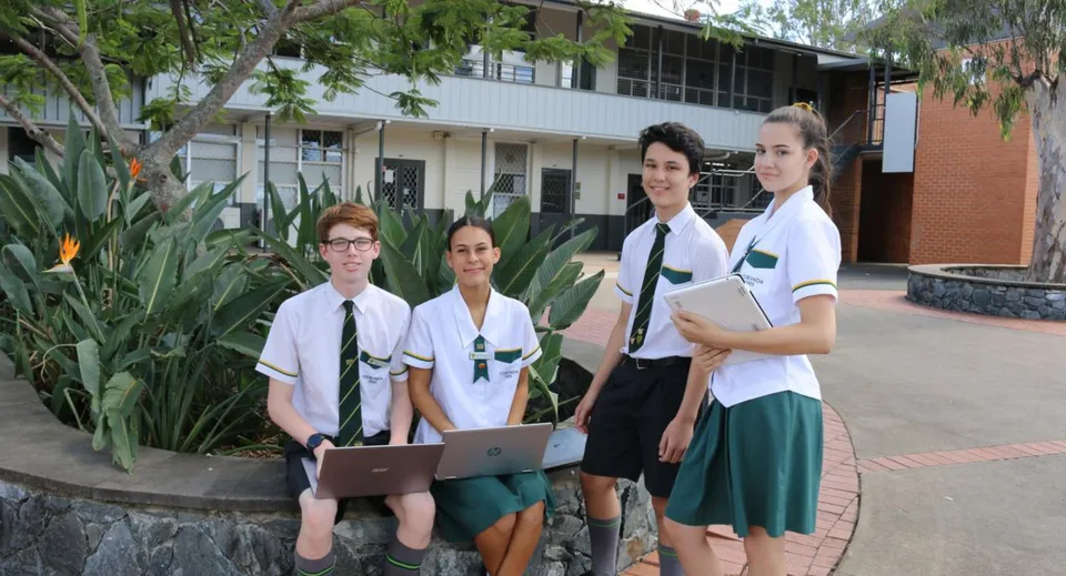 Quattro studenti della Corinda State High School sono in piedi davanti all'edificio scolastico circondati da una verde vegetazione.