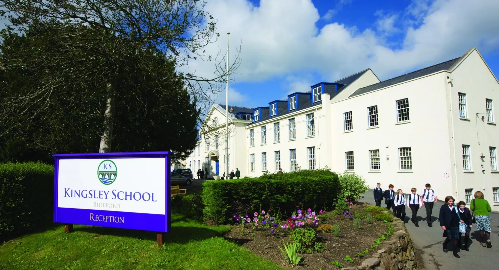 L'edificio bianco a più piani della Kingsley School è circondato da alberi e mostra un sentiero con persone sullo sfondo.