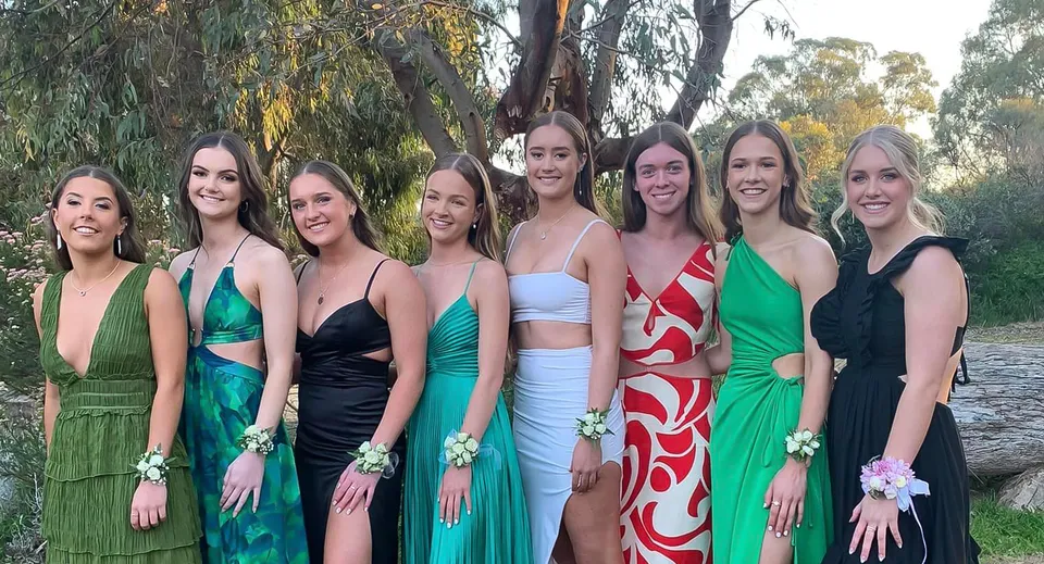 Un gruppo di giovani donne in abiti colorati insieme nel terreno della Kapunda High School davanti agli alberi.