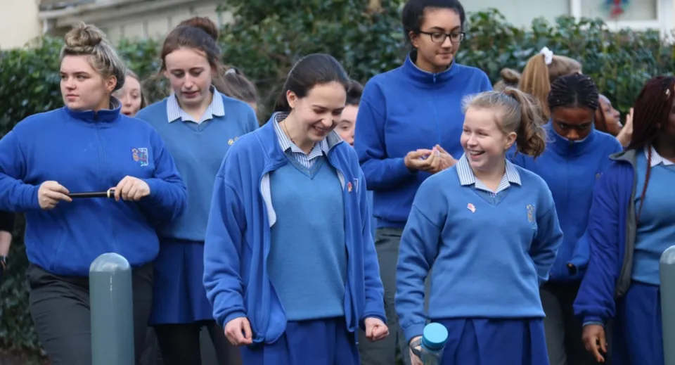 Un gruppo di studenti della Ursuline Secondary School a Cork si trova all'aperto davanti ad alberi ed edifici.