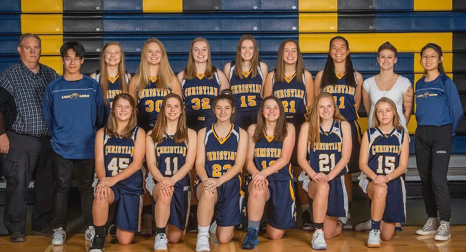 Un gruppo di giovani giocatrici di pallacanestro posa davanti a uno sfondo colorato giallo e blu nel campus della Colorado Springs Christian School.