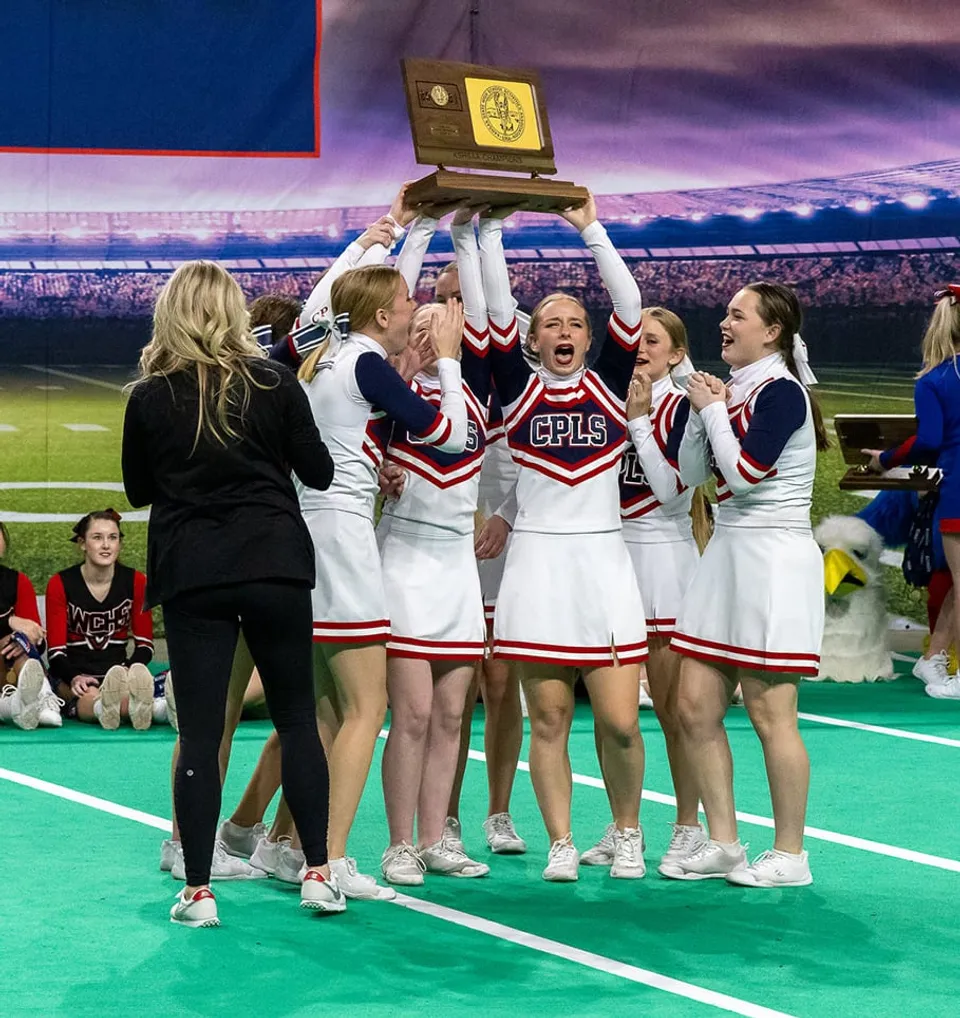 Le cheerleader della Cair Paravel Latin School festeggiano sul campo sportivo davanti a una grande folla.