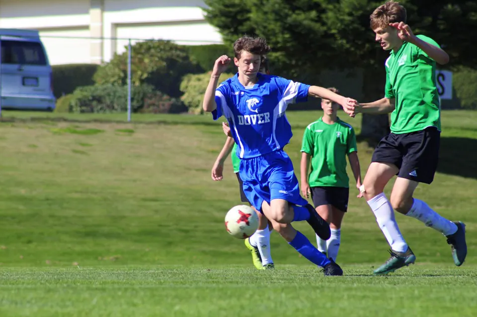 Due studentesse della Dover Bay Secondary School giocano a calcio su un campo verde davanti a una porta.