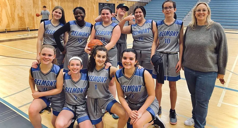 Gruppo di studentesse della Belmont Secondary School in divisa da basket all'interno di una palestra.