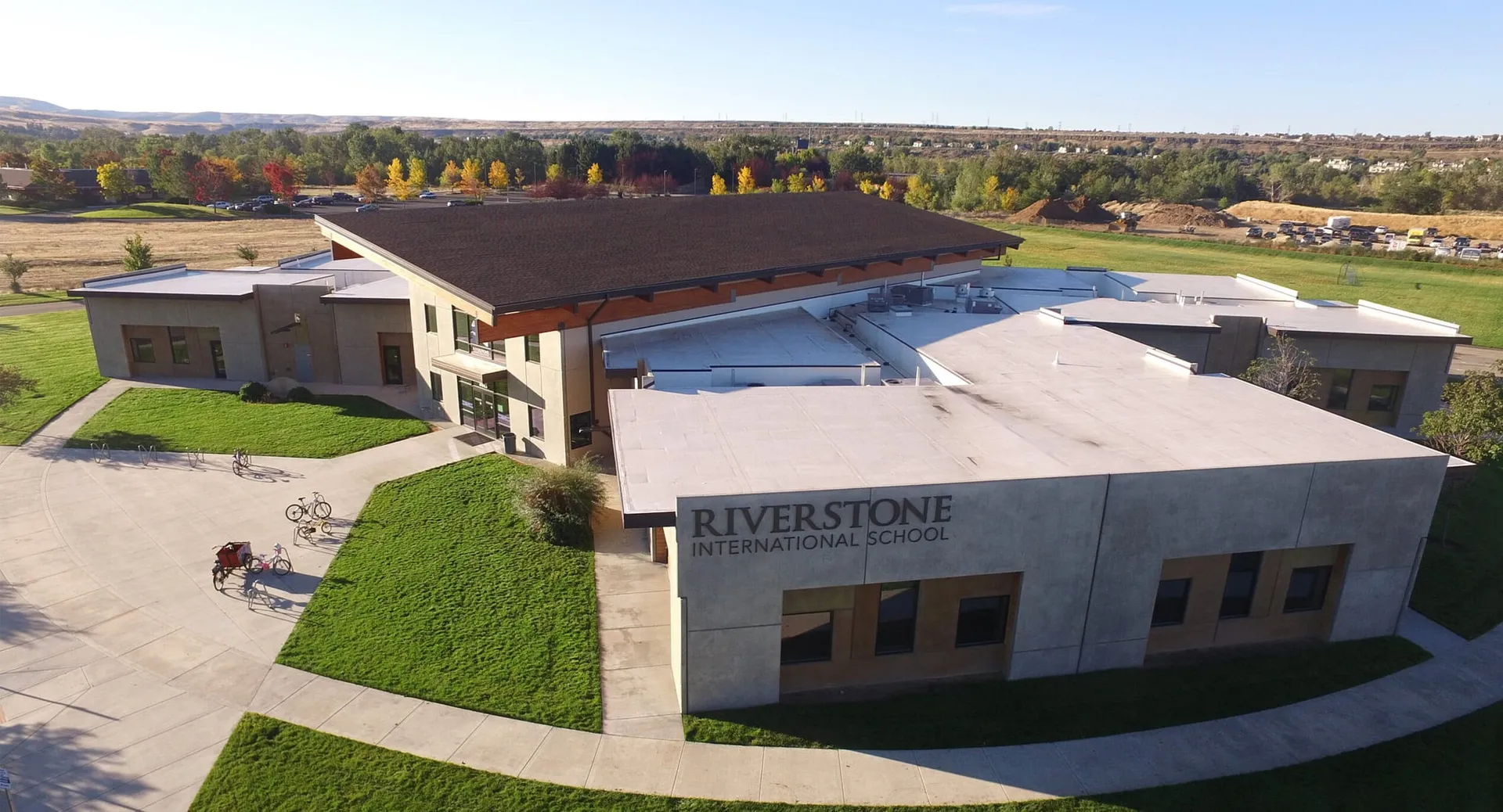 L'edificio scolastico moderno della Riverstone International School si trova su un campus erboso con un bosco sullo sfondo.