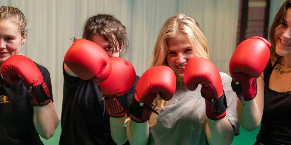 Quattro studentesse della École Jeannine Manuel posano con guantoni da boxe rossi davanti a una tenda.